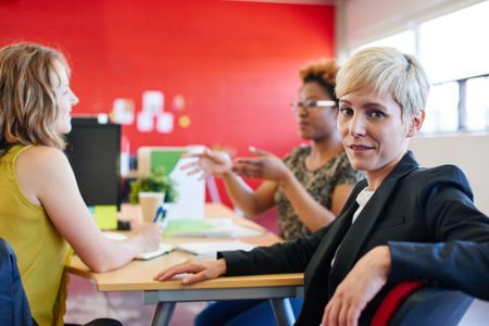 Confident female designer sitting at her desk for a brainstorming in red creative office space