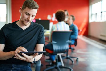 Confident male designer working on a digital tablet in red creative office space