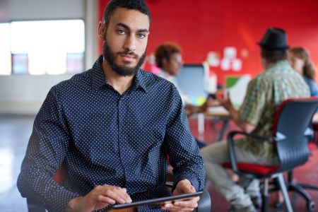 Confident male designer working on a digital tablet in red creative office space