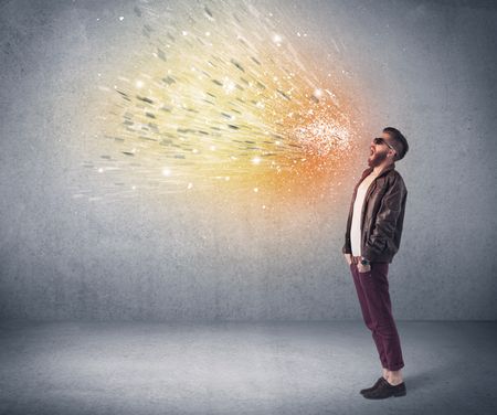 A young hipster guy with beard and sunglasses shouting in front of urban wall with vomit like colorful paint splatter on wall concept