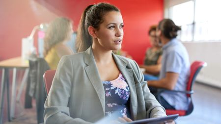 Confident female designer working on a digital tablet in red creative office space