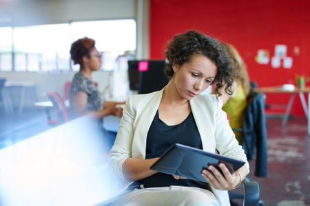 Confident female designer working on a digital tablet in red creative office space