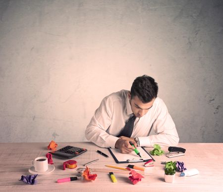 A young office worker sitting at desk working with keyboard, papers, highliter in front of empty clear background wall concept