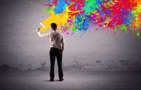 An elegant businessman in suit painting colorful splatter, bright colors on grey urban wall with a paint roller in his hand concept