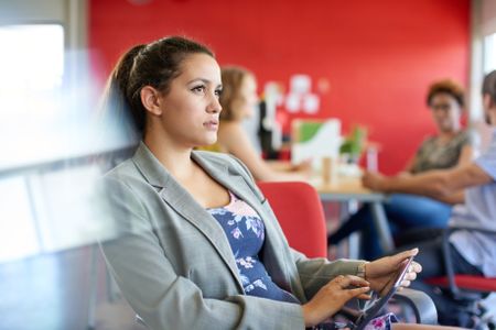 Confident female designer working on a digital tablet in red creative office space