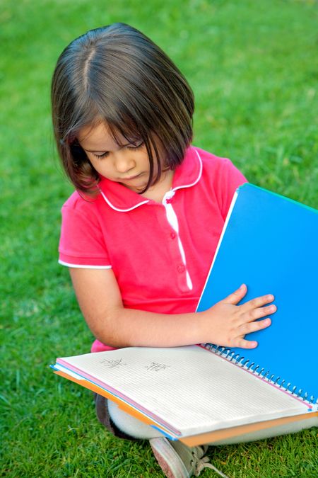 Little girl portrait reading a notebook outdoors