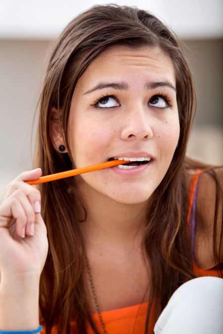 Pensive female student with a pencil on her mouth