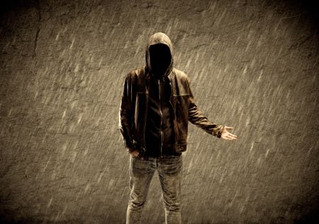 A strange suspicious confident hacker standing with a hoodie and leather jacket in front of sepia brown urban concrete wall concept