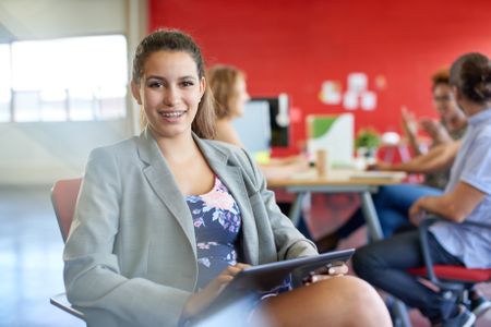 Confident female designer working on a digital tablet in red creative office space