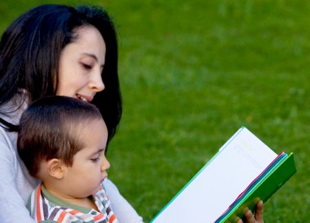 Mother reading a book to her son outdoors