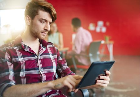 Confident male designer working on a digital tablet in red creative office space