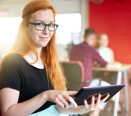 Confident female designer working on a digital tablet in red creative office space