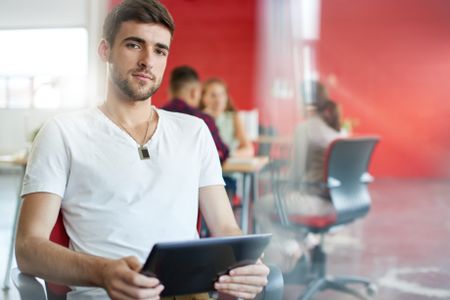 Confident male designer working on a digital tablet in red creative office space