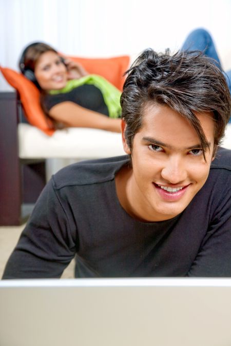 young man smiling on his laptop at home with his girlfriend behind him