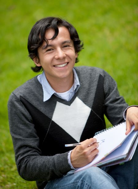Male student with a notebook outdoors smiling
