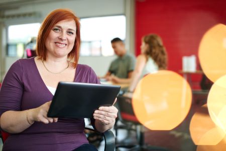Confident female designer working on a digital tablet in red creative office space