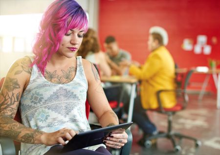 Confident and edgy female designer working on a digital tablet in red creative office space