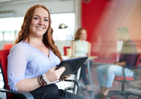Confident redhead female designer working on a digital tablet in red creative office space