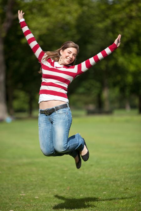 Casual excited girl jumping outdoors and smiling
