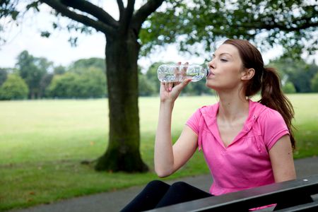 sporty woman resting on a bench drinking water