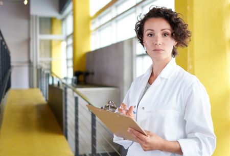 Portrait of a female doctor holding her patient chart in bright modern hospital