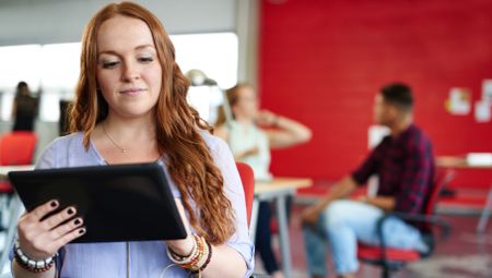 Confident redhead female designer working on a digital tablet in red creative office space