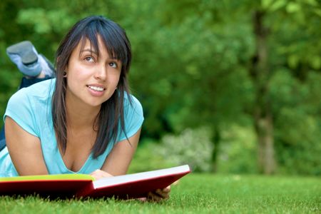 Happy student laying on the floor outside with a book