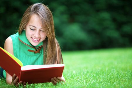 Beautiful girl smiling reading a book outdoors