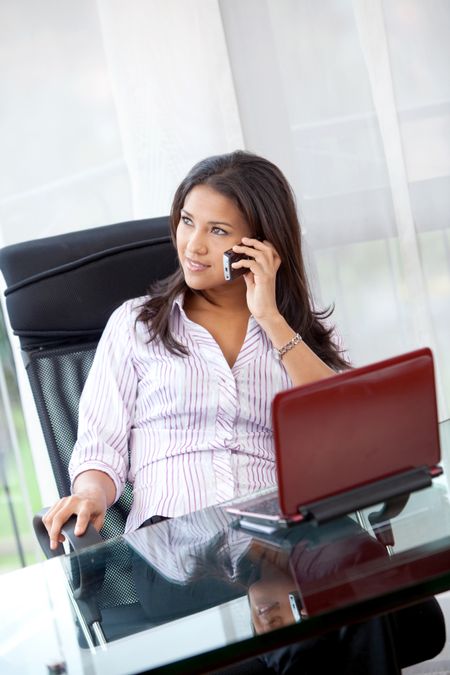 Young business woman with a laptop talking on the phone indoors