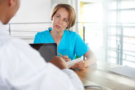 Team of doctor and nurse discussing a patient diagnosis sitting at the desk in bright modern office