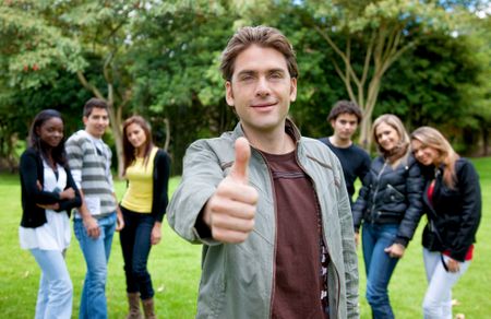 Man with thumbs up outdoors and a group behind him