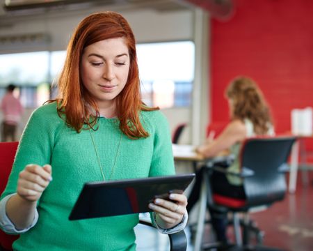 Confident female designer working on a digital tablet in red creative office space