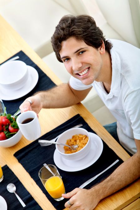 Handsome man eating cereals at breakfast and smiling