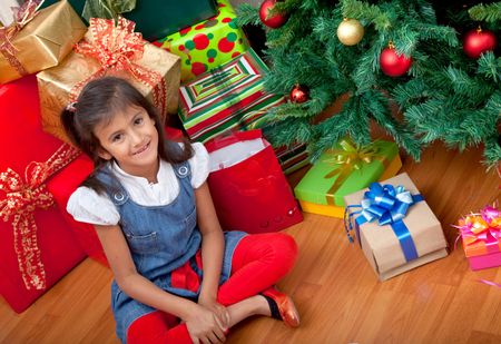 Happy girl next to a Christmas tree surrounded by gifts