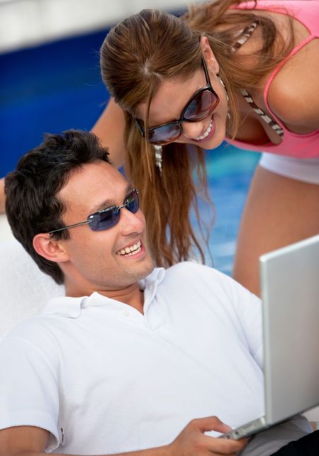 couple using a laptop while relaxing by the swimming pool