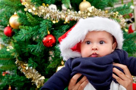 Cute baby with Santa hat and christmas tree behind