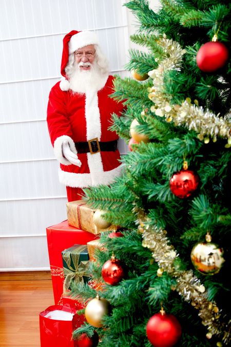 Santa Claus with a christmas tree and gifts indoors
