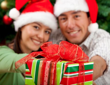 Christmas couple smiling next to a tree with a present