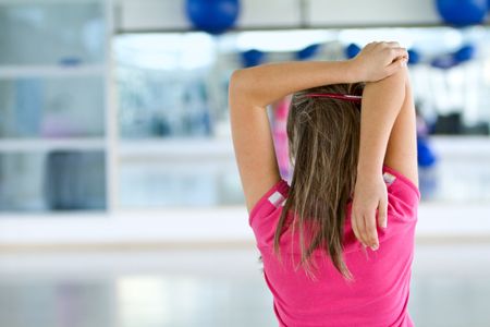 Woman doing stretching exercises for her arm and back at the gym
