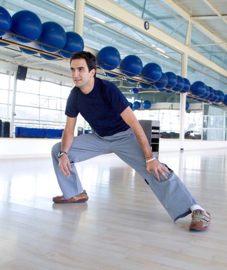 Happy young man doing stretching exercises at the gym