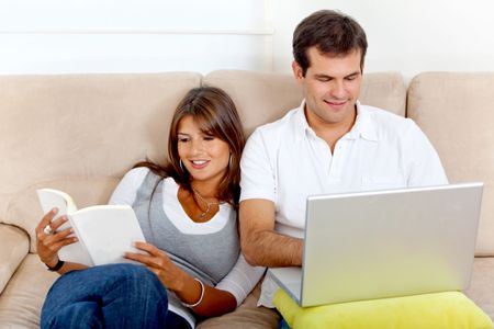 Beautiful couple resting with a laptop and reading a book indoors