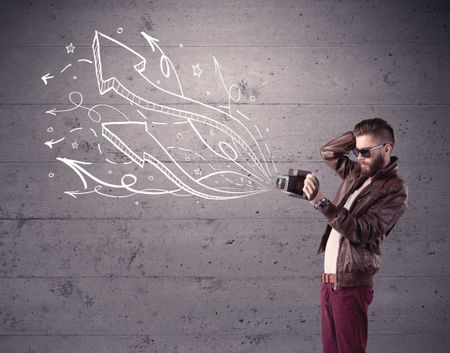 A hipster guy opening his point of view through looking a vintage camera concept with illustratied drawn arrows on urban wall