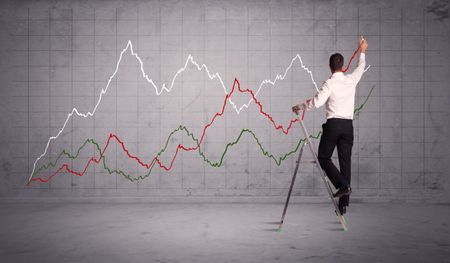 A guy in modern suit standing on a small ladder and drawing a chart on grey wall background with exponential progressing curves, lines