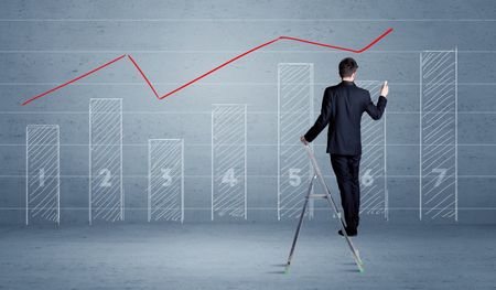 A man in elegant suit standing on a small ladder and drawing a chart on blue wall background with numbers, lines, blocks,