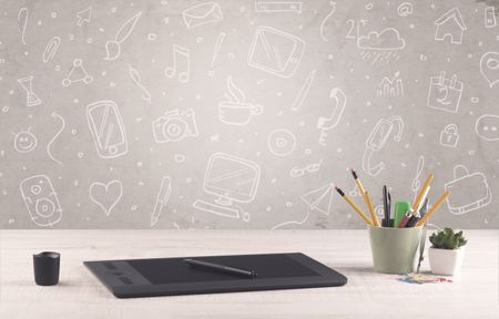 Close up of business office desk with laptop tablet in front of brown wall background full of drawn communication icons and school items concept