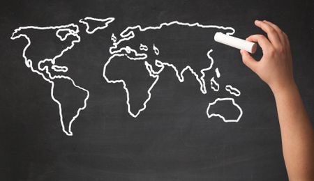 A teacher drawing the map of the world on a blackboard with a chalk
