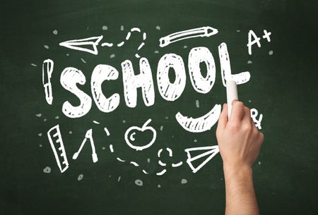 A teacher writing school, drawing children things on clean green chalkboard by hand