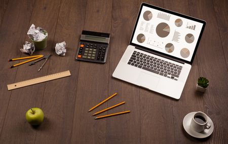 Pie chart graph icons and symbols on laptop screen with office accessories 