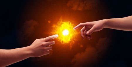 Two naked male hands about to touch, lighting a bright flame with smoke in red sky background concept