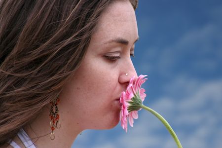 beautiful girl kissing a pink flower with a blue sky in the background